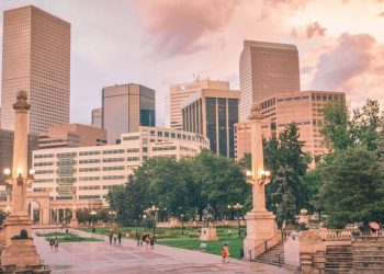 The Denver skyline and Civic Center Park at sunset, with historic monuments, green spaces, and downtown skyscrapers under colorful evening clouds.