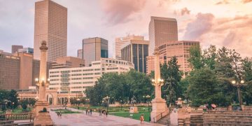 The Denver skyline and Civic Center Park at sunset, with historic monuments, green spaces, and downtown skyscrapers under colorful evening clouds.