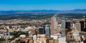 Aerial view of Downtown Denver with high-rise buildings, tree-lined streets, and mountains visible in the distance, surrounded by some of the best Denver neighborhoods.