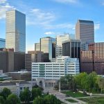 Aerial view of Downtown Denver with high-rise office buildings, a large green park, and dramatic clouds overhead, all common sights when you’re living in Denver.