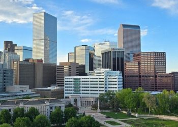 Aerial view of Downtown Denver with high-rise office buildings, a large green park, and dramatic clouds overhead, all common sights when you’re living in Denver.