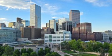Aerial view of Downtown Denver with high-rise office buildings, a large green park, and dramatic clouds overhead, all common sights when you’re living in Denver.