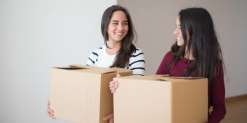 Two smiling students with moving boxes using college student storage solutions during a move.