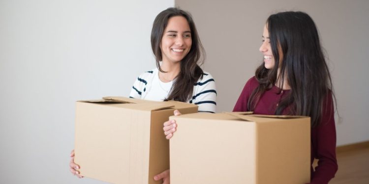 Two smiling students with moving boxes using college student storage solutions during a move.