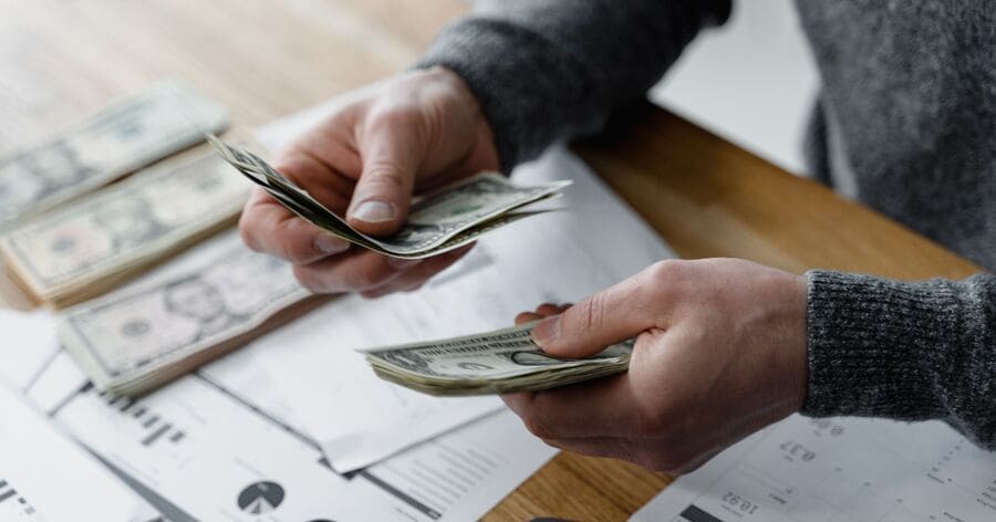 A person counts cash over financial documents and a calculator while budgeting for moving with a motorcycle.