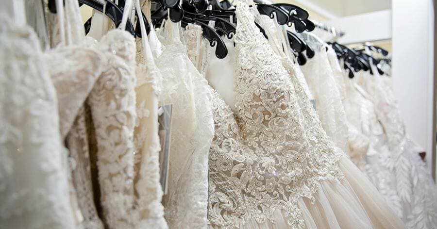 Close-up of a row of lace and embroidered wedding dresses displayed on hangers inside a bridal boutique showroom.