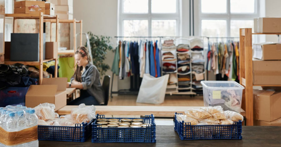 A woman is sitting at a desk in a large workspace, surrounded by racks of clothing and other items on freestanding shelves, which she uses for small-business storage.