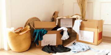 Three cardboard boxes labeled “keep,” “donate,” and “trash” with items of clothing hanging over the edges and a few pieces on the floor.