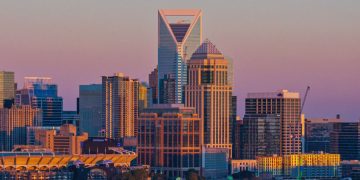 Charlotte skyline at sunset with Uptown skyscrapers and the Bank of America Stadium in the foreground.