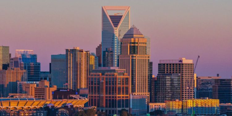 Charlotte skyline at sunset with Uptown skyscrapers and the Bank of America Stadium in the foreground.
