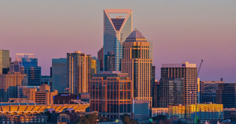 Charlotte skyline at sunset with Uptown skyscrapers and the Bank of America Stadium in the foreground.
