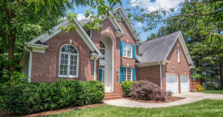 A large suburban home with a red brick exterior, two-car garage, and blue shutters.