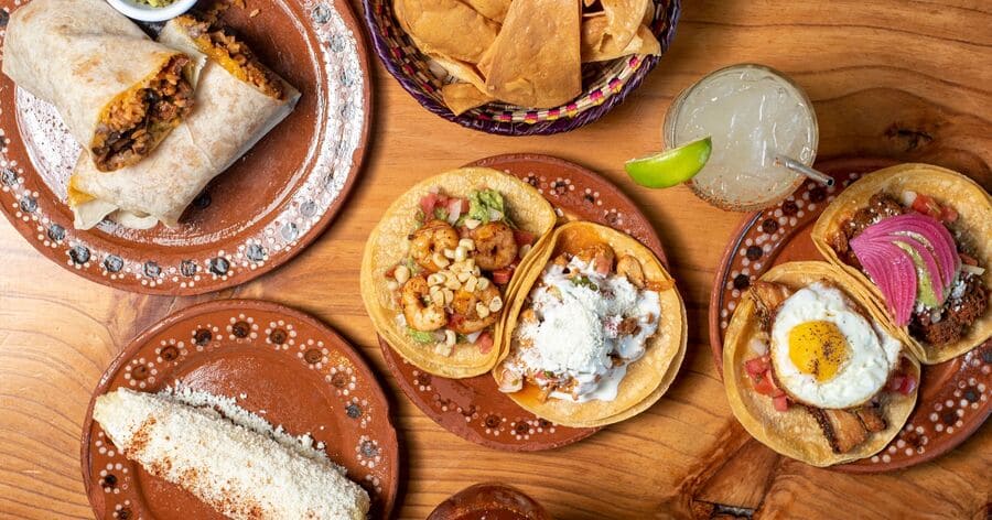Top view of tacos, burritos, street corn, chips, and margaritas on a restaurant table.
