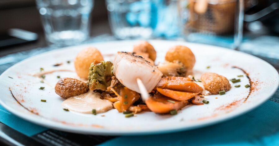A white plate with seared scallops, roasted vegetables, and a creamy sauce.