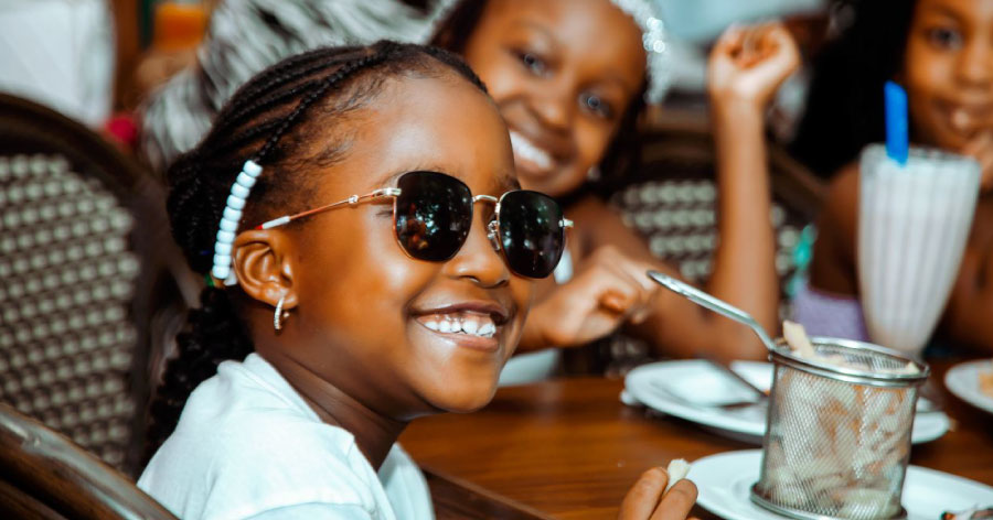Three young girls sitting at a restaurant table are smiling for a picture while they enjoy french fries and milkshakes.