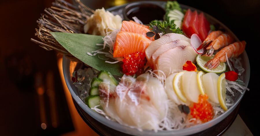 Fresh sashimi platter with salmon, white fish, shrimp, cucumber, and garnishes served over ice.