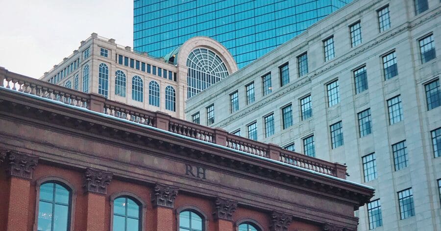 A historic brick building framed by modern glass and stone office towers, highlighting the blend of old and new architecture found while living in Boston.
