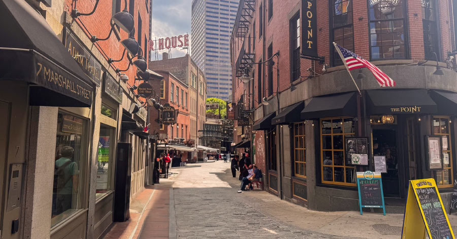 Sunny daytime view down Marshall Street featuring brick storefronts in Haymarket, one of the best neighborhoods in Boston for tourists to visit.