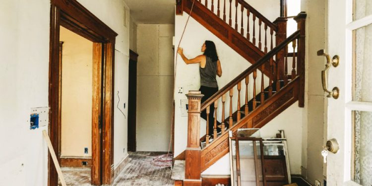 A woman is inspecting a wall in her house, which is mostly empty thanks to home renovation storage.