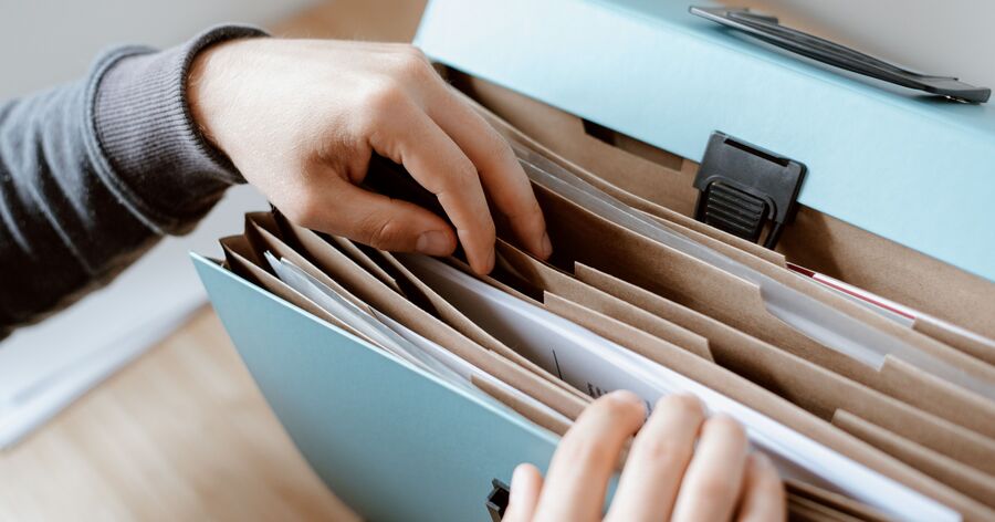 A person organizes important documents inside a portable file box to keep moving paperwork secure and accessible.