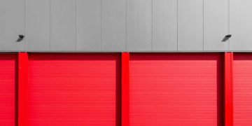 Exterior of a storage facility, like CubeSmart, with bright red roll-up storage unit doors.